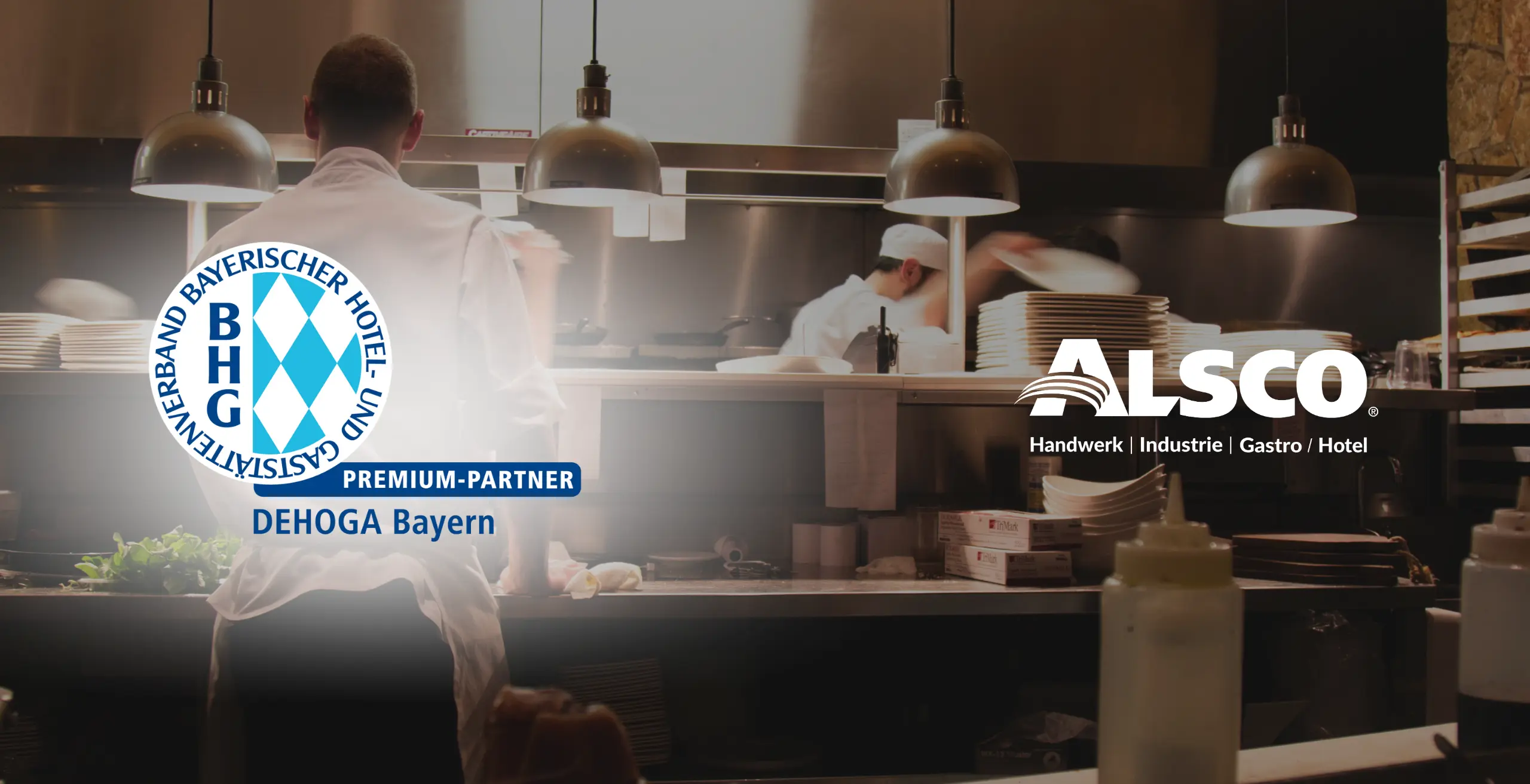 Also und DEHOGA Bayern Premiumlogo vor dem Hintergrund einer Restaurantkรผche